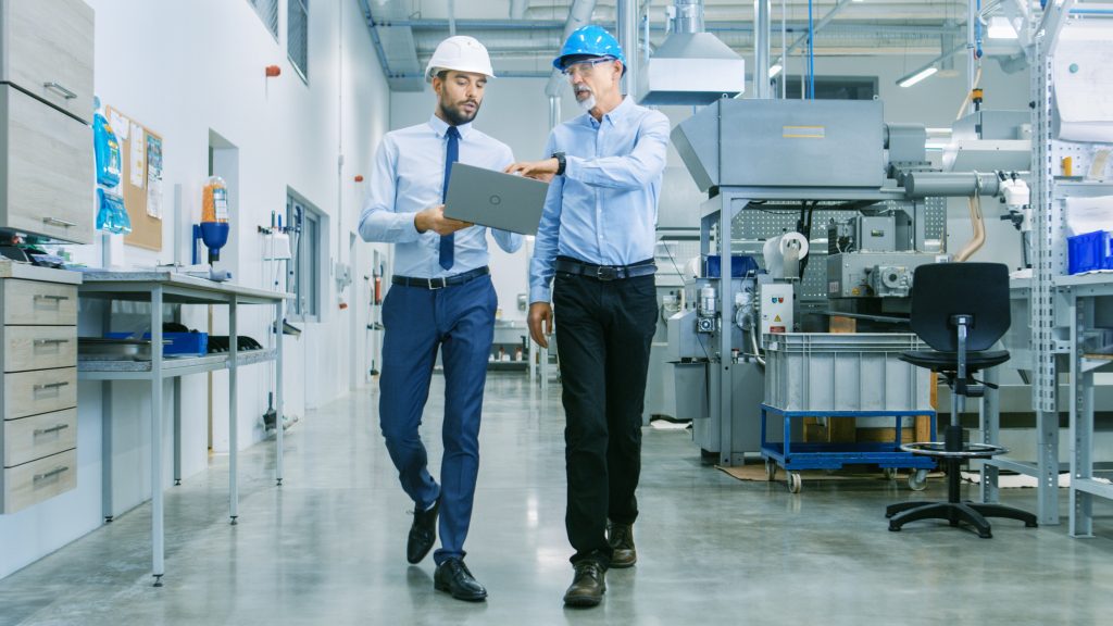 Two men wearing hard hats walking around a manufacturing facility during an audit.