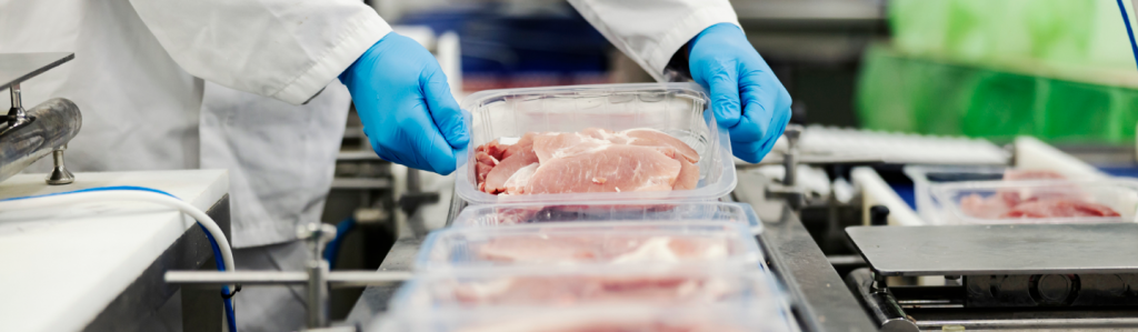 Factory worker wearing gloves and holding a package of poultry. BRC certification is common for meat processors such as this.