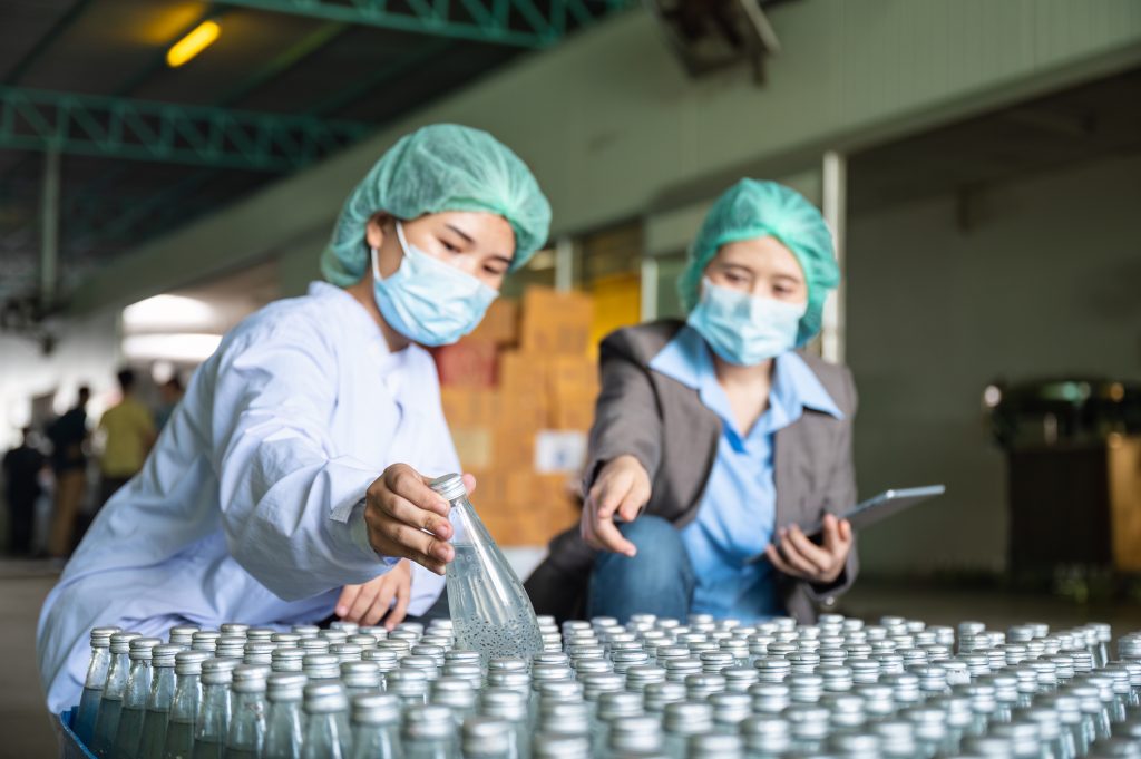 Quality Assurance managers inspecting glass bottles in a bottling factory demonstrating CAPA.