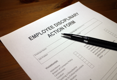 Employee Disciplinary Action Form with violation check boxes, sitting on a table with a black pen.