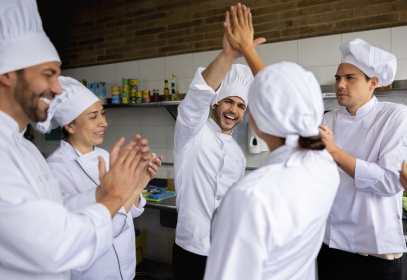 A group of chefs in a kitchen high-fiving to celebrate food safety culture.