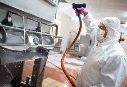 Man spraying chemicals on a machine in a food factory.